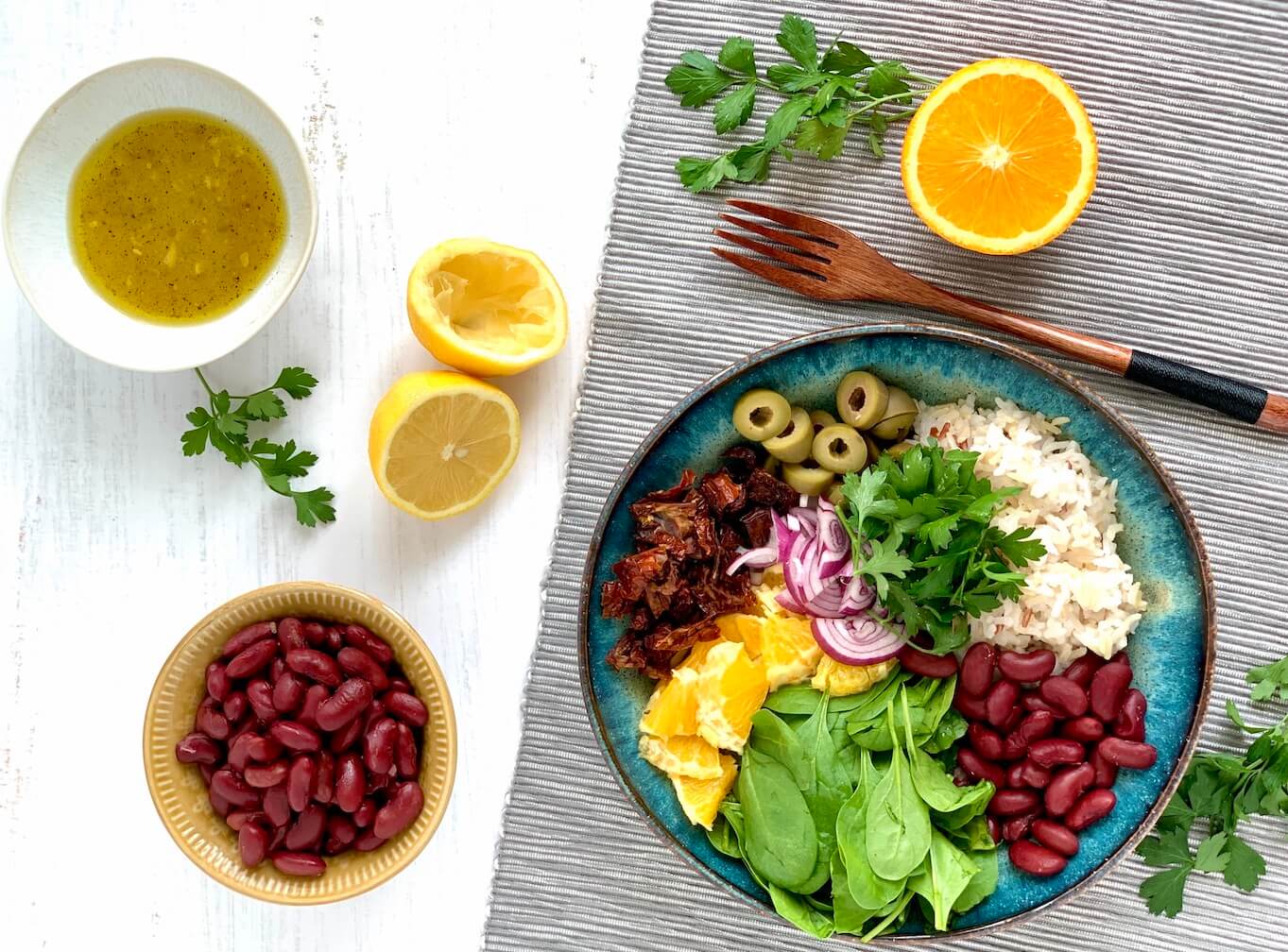 vegan Buddha bowl with whole foods, brown rice, kidney beans, spinach, orange, olives, red onion, sun-dried tomatoes, lemon, parsley